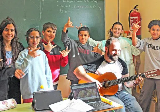El docente Miguel Lucia toca la guitarra mientras varios de sus alumnos de Primaria hacen el gesto de los cuernos rockeros.