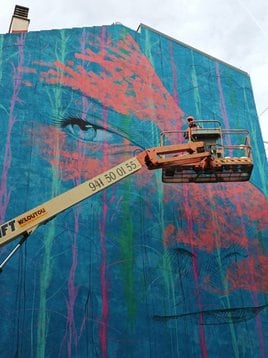 El artista Carlos Callizo pinta un mural en una fachada de Lardero. En detalle, Callizo saluda desde la grúa.