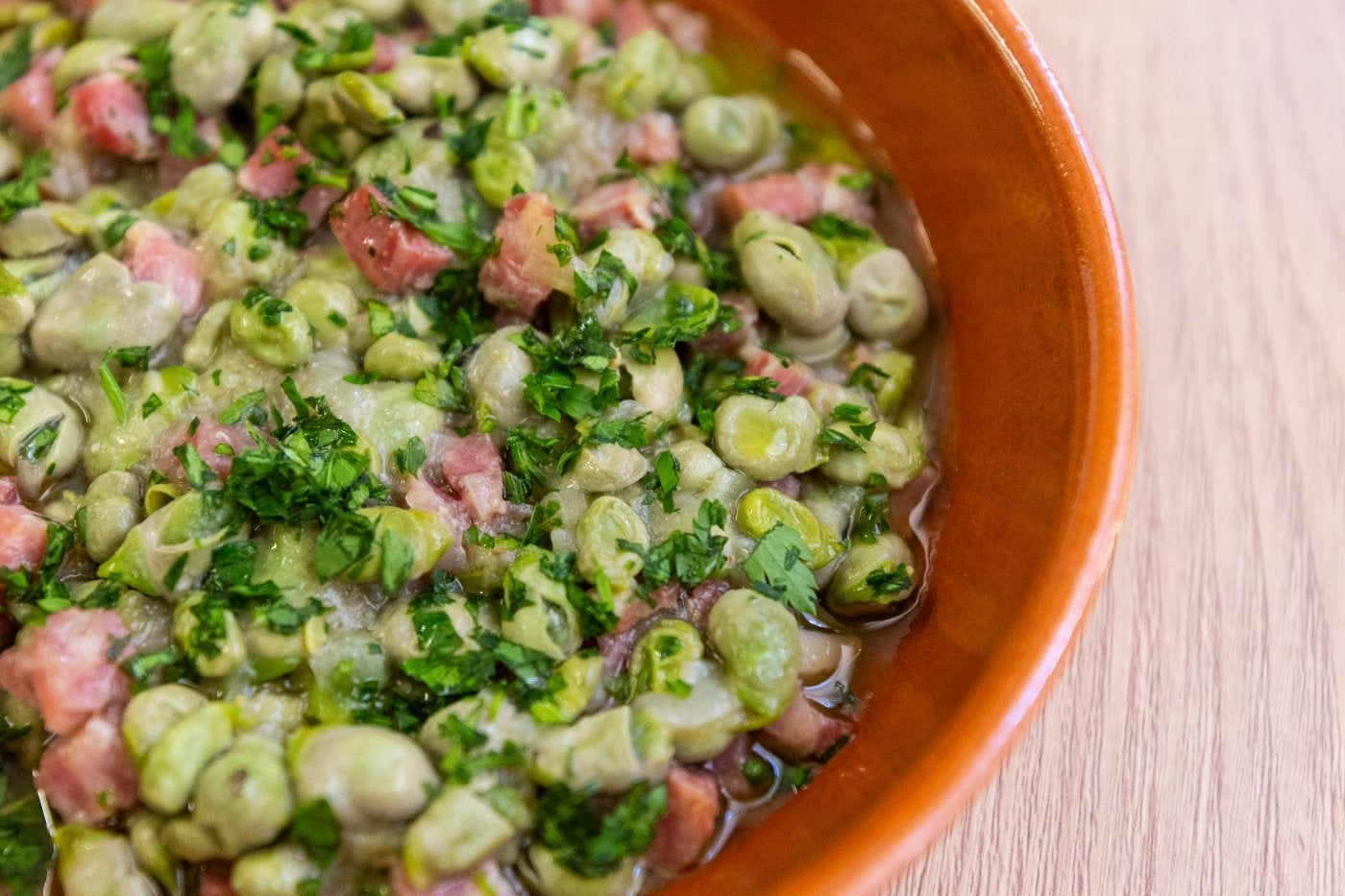 Un plato de barro con habas frescas con jamón.