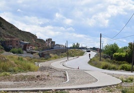 Una mujer asciende en patinete el reconstruido puente de la avenida del Camino Real sobre la AP-68 mientras una furgoneta lo desciende.