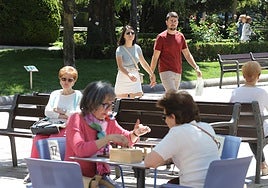 Una pareja pasea por El Espolón mientras dos mujeres juegan al ajedrez.