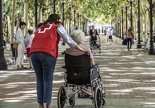 Una voluntaria de Cruz Roja acompaña a una persona mayor en silla de ruedas.