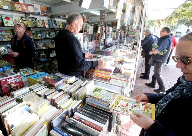 Varias personas curiosean entre algunas de las propuestas literarias de uno de los puestos.