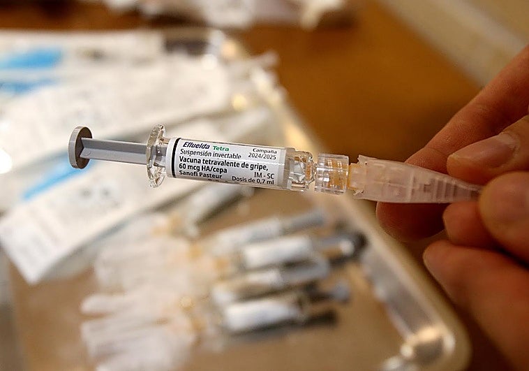 Un profesional sanitario prepara la jeringuilla con la vacuna antigripal para inmunizar a un residente en un centro de mayores.