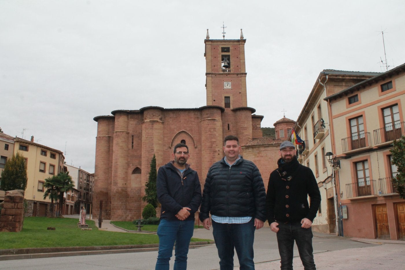 Robles y Perrino, de Cluny Ibérica, posan junto al alcalde Salaverri (centro) con el monasterio al fondo.