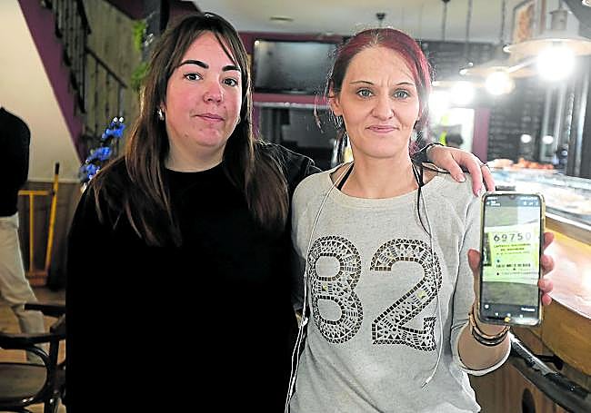 Mirian, camarera del bar Tôlmay, junto a su compañera Raquel, muestra el décimo no premiado que terminó comprando en la misma administración.