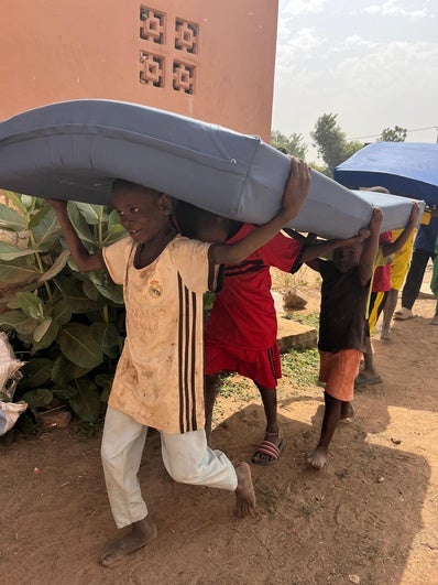 Un grupo de niños senegaleses portan los colchones que ha llevado la ONG.