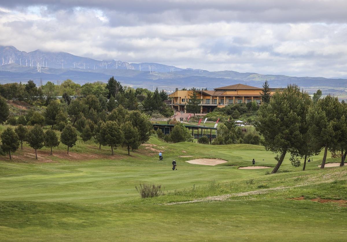 Varios jugadores avanzan por la calle de uno de los hoyos, en una vista panorámica del campo y la Casa Club.