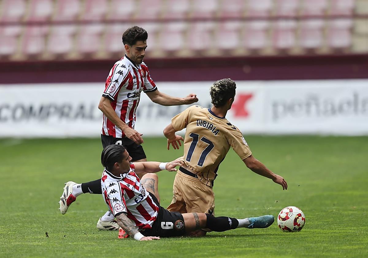 Lamadrid y Castañeda, desde el suelo, intentan arrebatarle el balón a Zubiria, del Eibar B.