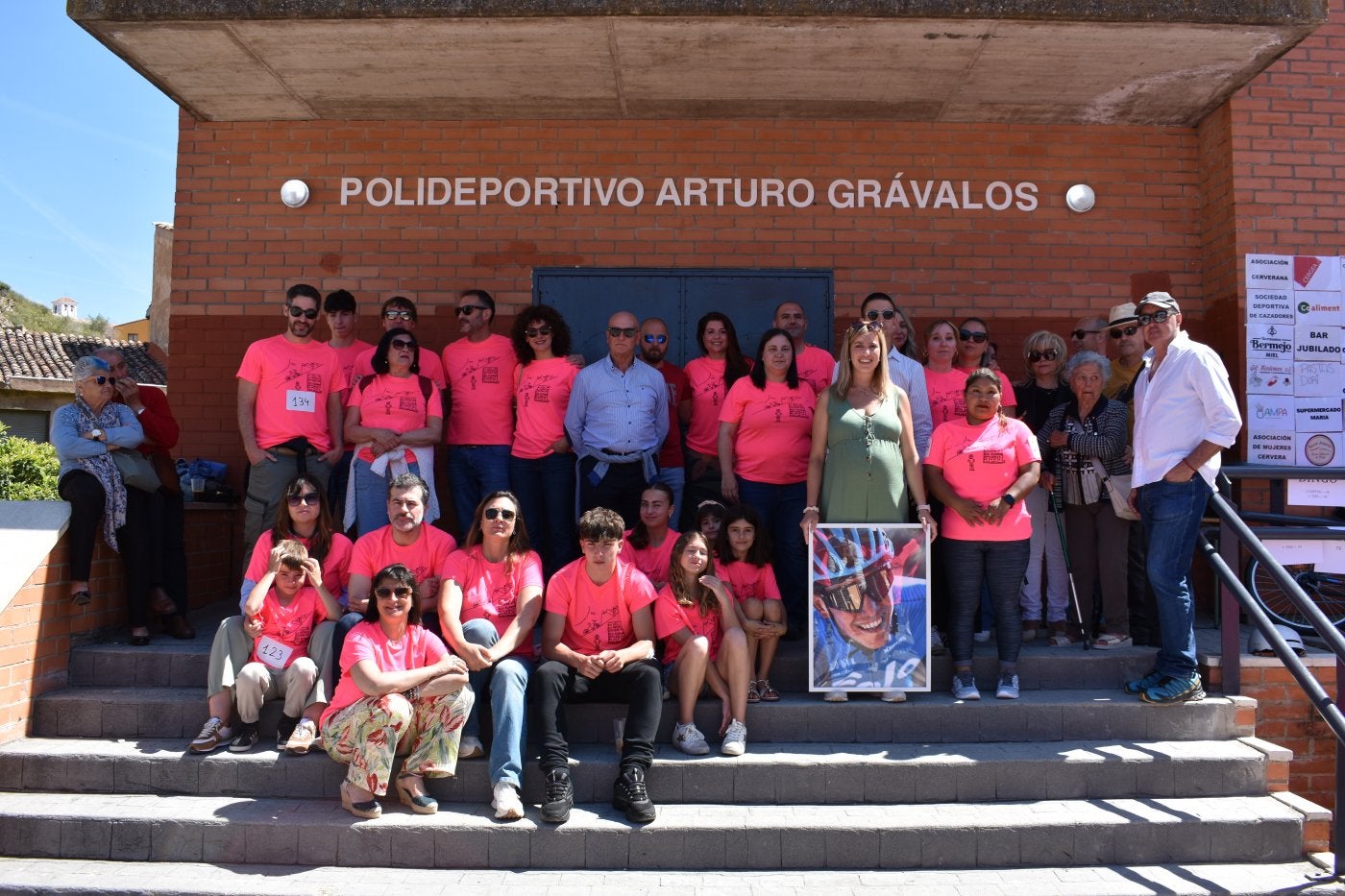 Familia de Arturo Grávalos, autoridades e integrantes de la AMPA junto a la entrada del polideportivo de Cervera, con una foto del ciclista.