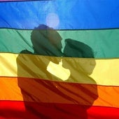 Una pareja de mujeres se besa tras la bandera LGTBI.