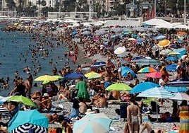 Una multitud bajo el sol en una playa, en la que muchos turistas, no obstante, se protegen bajo sombrillas.