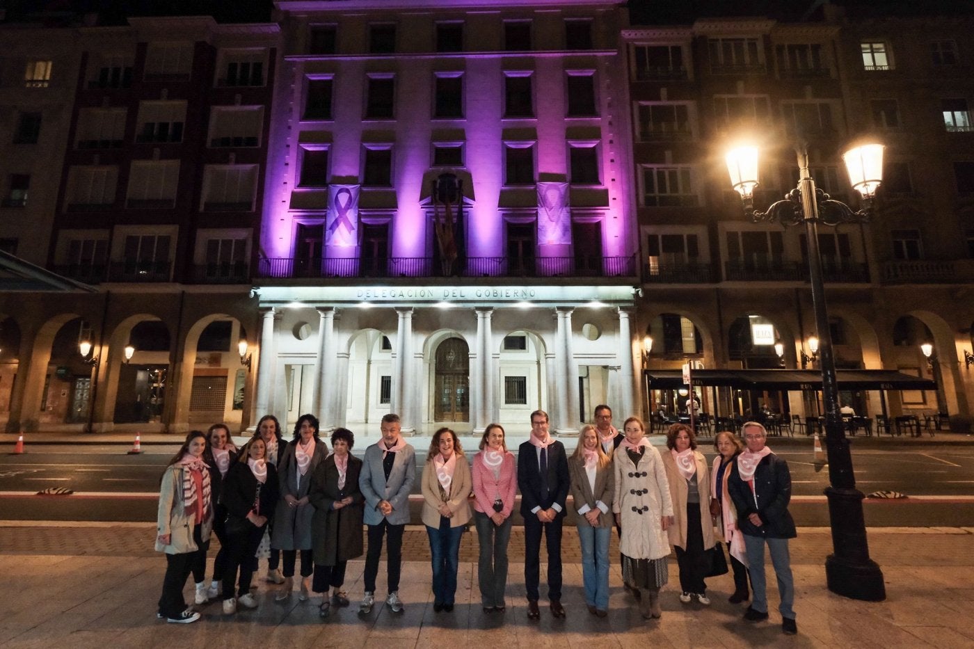 Varios representantes de la política riojana frente al edficio de la Delegación del Gobierno iluminado de rosa.
