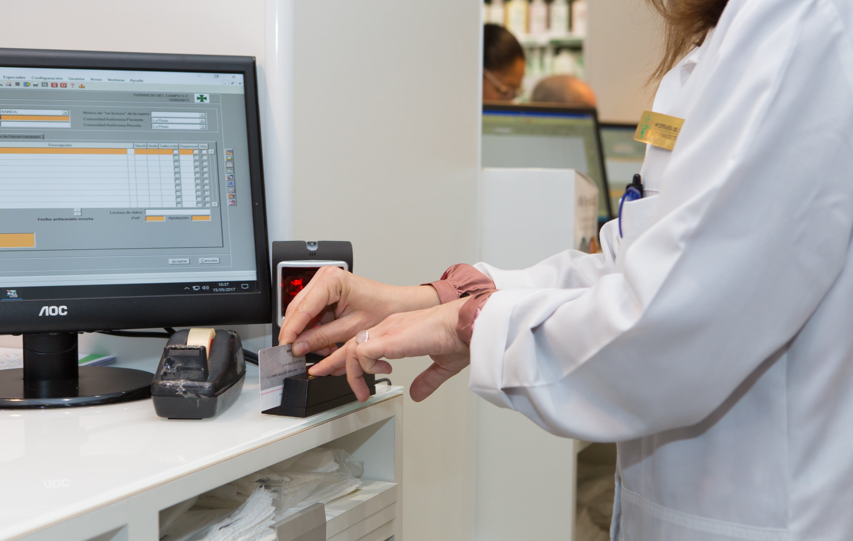 Una farmacéutica pasa por el lector la tarjeta sanitaria de un paciente para comprobar la medicación disponible en el sistema de receta electrónica.