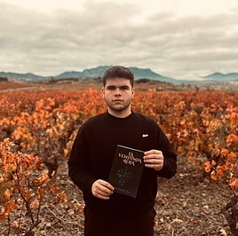Sergio Pereda con su libro en la mano ante un viñedo otoñal.