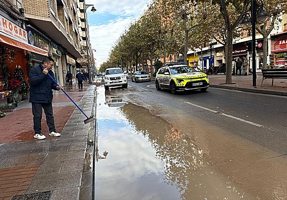 Un comerciante achica el agua de la acera junto a su tienda.