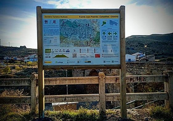 Sendero con la señal de dirección y panel con la ruta situado junto al puente medieval de Igea.