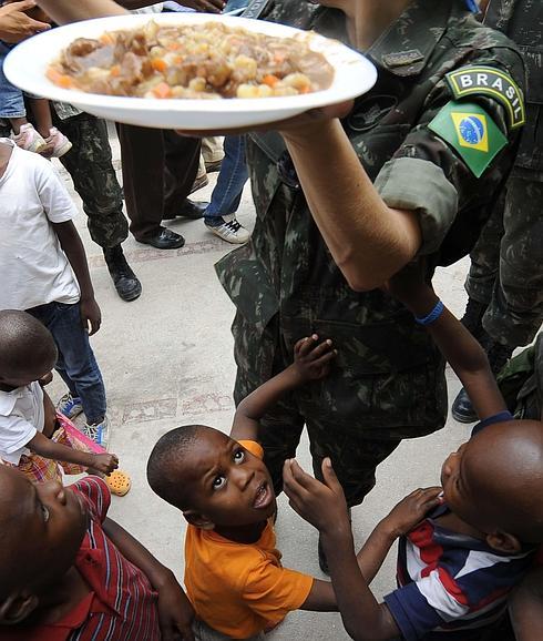 Niños haitianos esperan un plato de comida de las manos de un soldado brasileño 