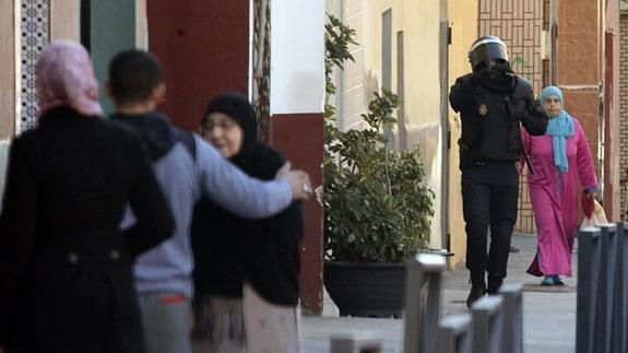 Un policía pasa junto a varios vecinos de la barriada de El Príncipe. 