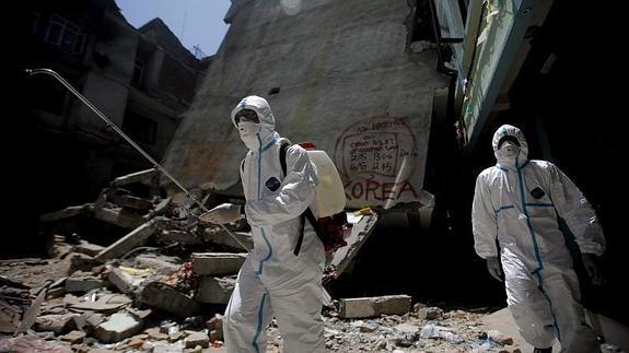 Un voluntario nepalí esparce desinfectante en los restos de un edificio.