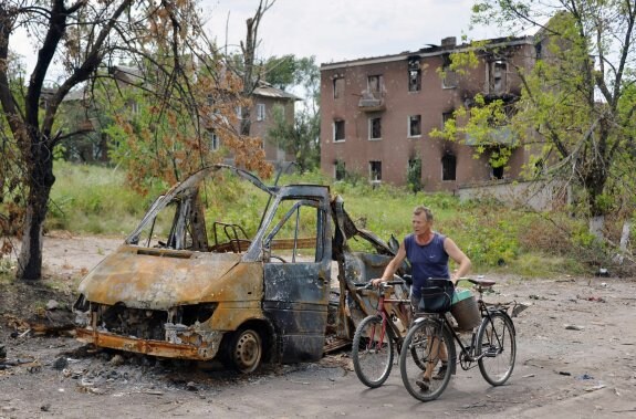 Un hombre camina por una calle de la región de Donetsk en la que se aprecia un vehículo calcinado. 