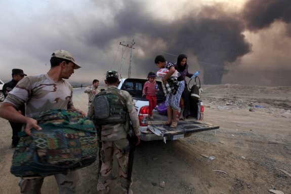 Los soldados iraquíes ayudan civiles en la ciudad Qaraqosh, mientras arden los pozos petrolíferos incendiados por el EI. :: x. Al-Marjani / Reuters
