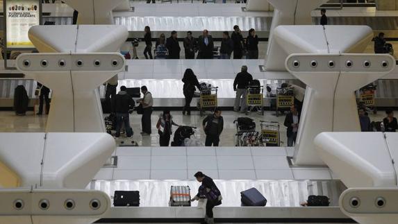 Los pasajeros de un aeropuerto aguardan la salida de sus equipajes en las cintas transportadoras. 