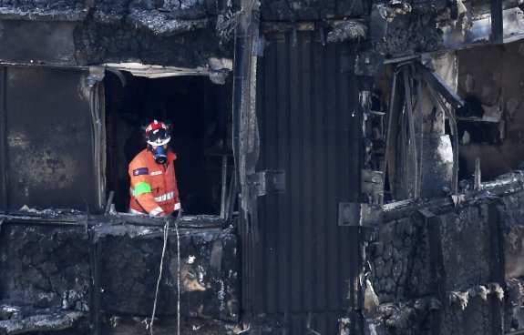 Un bombero examina la fachada carbonizada de la torre Grenfell. Abajo, otro bloque revestido de aluminio en Camden. :: efe y reuters
