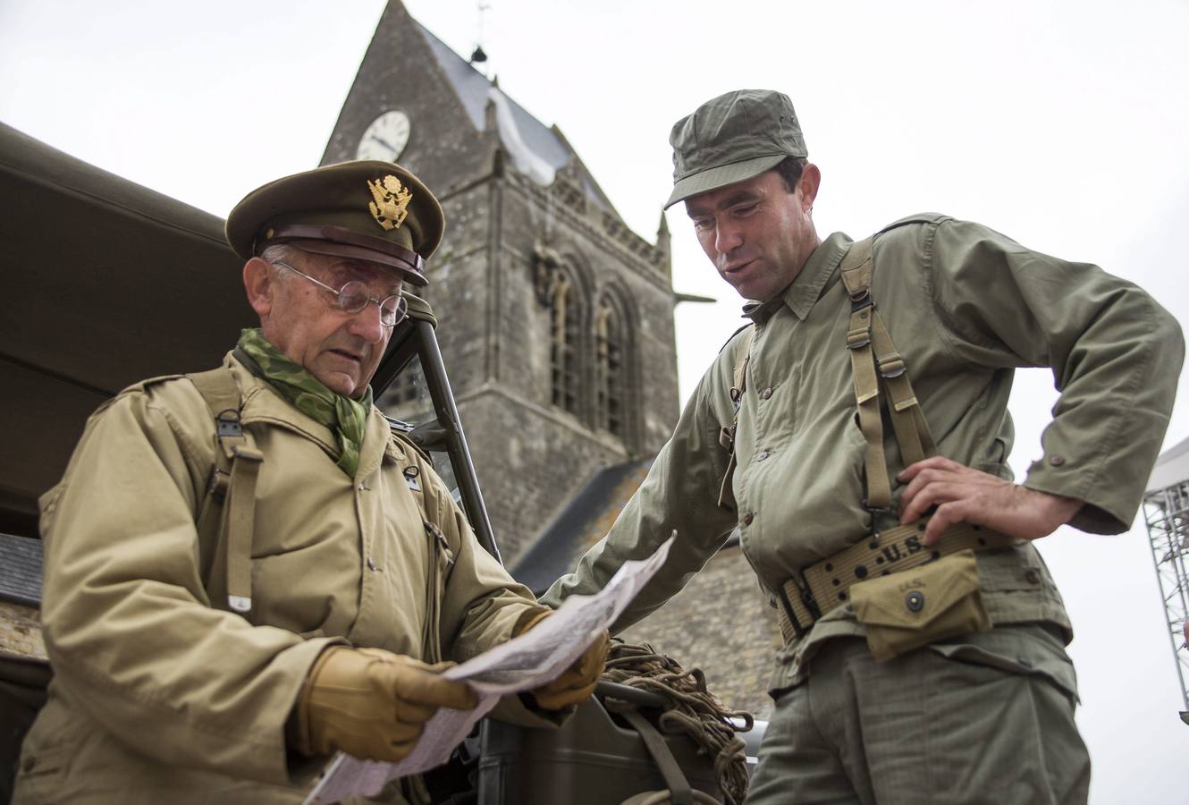 Dos entusiastas franceses de la Segunda Guerra Mundial, con uniformes réplica de los de la Segunda Guerra Mundial, se reúnen frente a la iglesia de Sainte-Mere-Eglise.