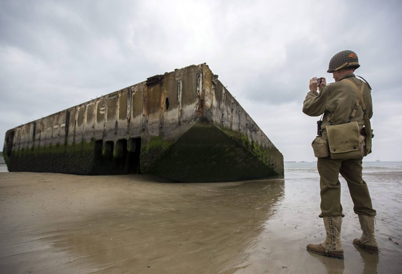 Un entusiasta de la Segunda Guerra Mundia, con una réplica del uniforme estadounidense, fotografía las ruinas del pontón de desembarco en la playa de Arromanches.