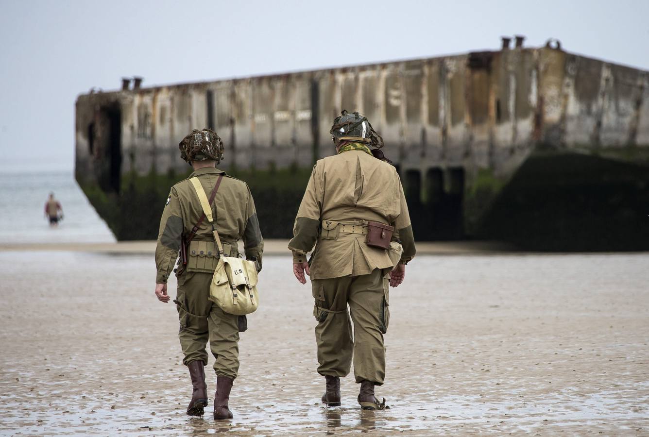 Varios entusiastas de la Segunda Guerra Mundial, con réplicas de uniformes estadounidenses de la época, caminan cerca de las ruinas del pontón de desembarco en la playa de Arromanches.