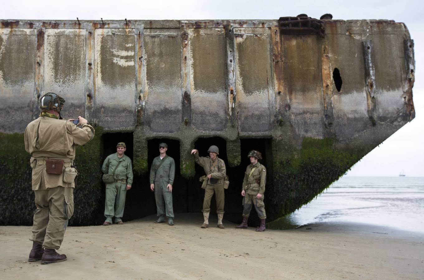 Varios entusiastas de la Segunda Guerra Mundial, con réplicas de uniformes estadounidenses de la época, se fotografían los unos a los otros en las ruinas del pontón de desembarco en la playa de Arromanches.