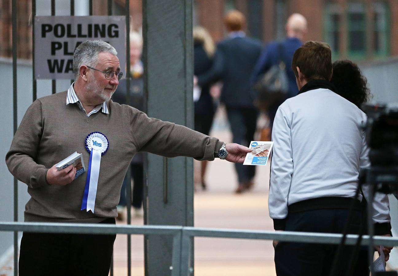 Escocia ya decide su futuro. Un hombre, defensor del 'sí' reparte papaletas antes de entrar en uno de los colegios electorales.