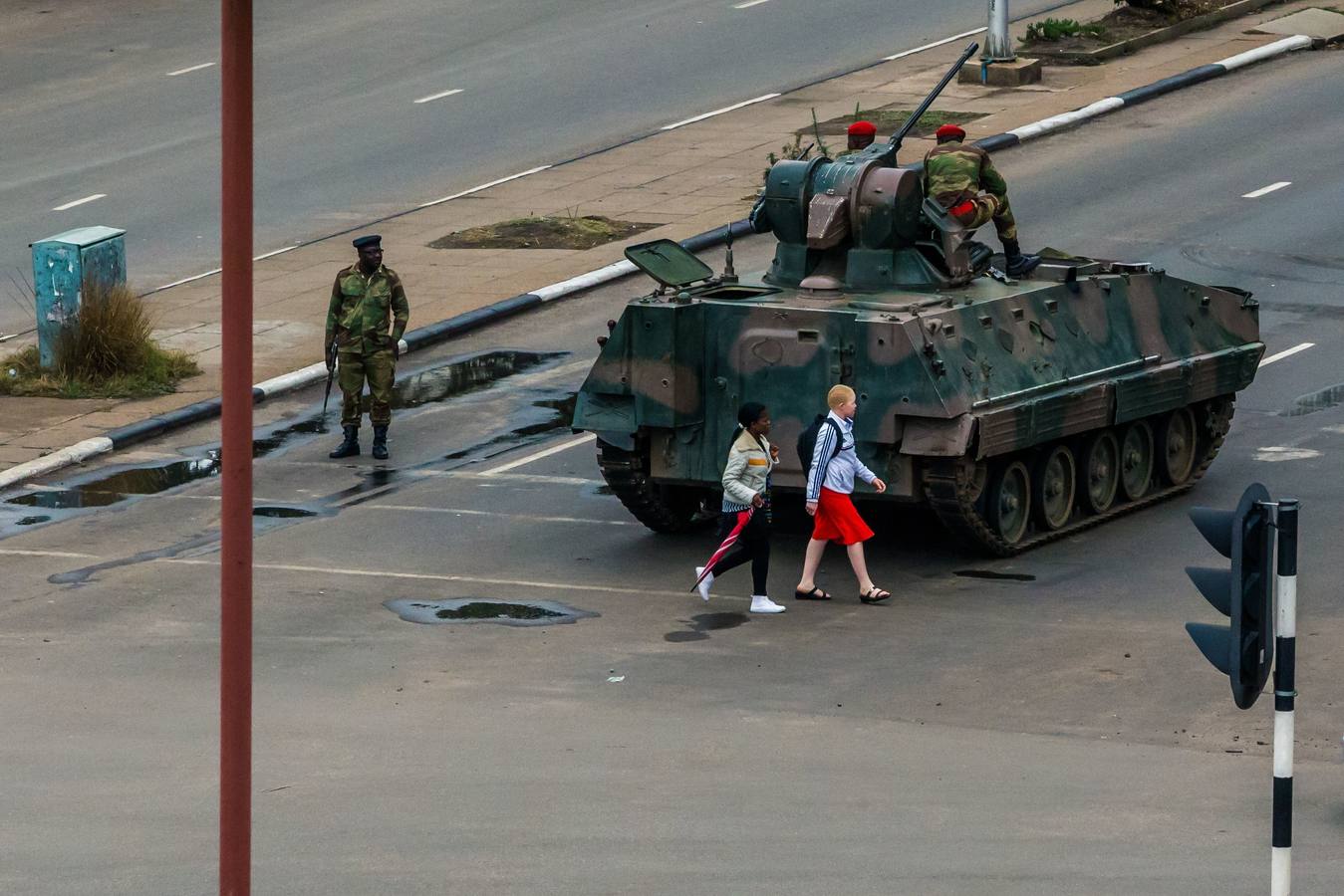 Dos jóvenes pasan junto a un tanque y soldados armados que regulan el tráfico en Harare. Las Fuerzas Armadas de Zimbabue se han hecho con el control del país tras poner bajo arresto domiciliario al presidente, Robert Mugabe, que lleva 37 en el poder, prepara su dimisión y negocia la salida del país de su mujer. 