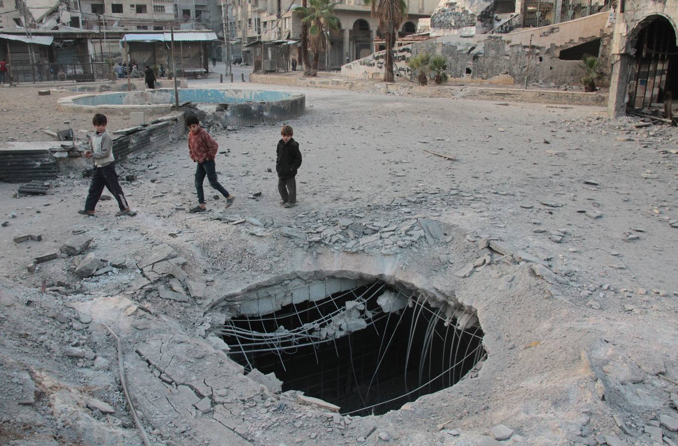 Unos niños pasan junto a un agujero causado por un ataque en la ciudad siria de Douma, en manos de los rebeldes. 