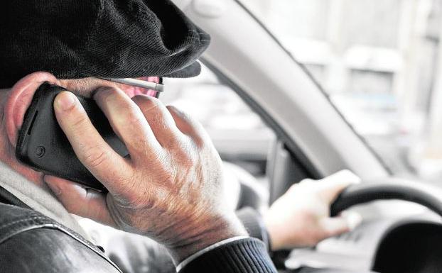 Un hombre conduce con una mano en el volante y otra en el teléfono móvil. 