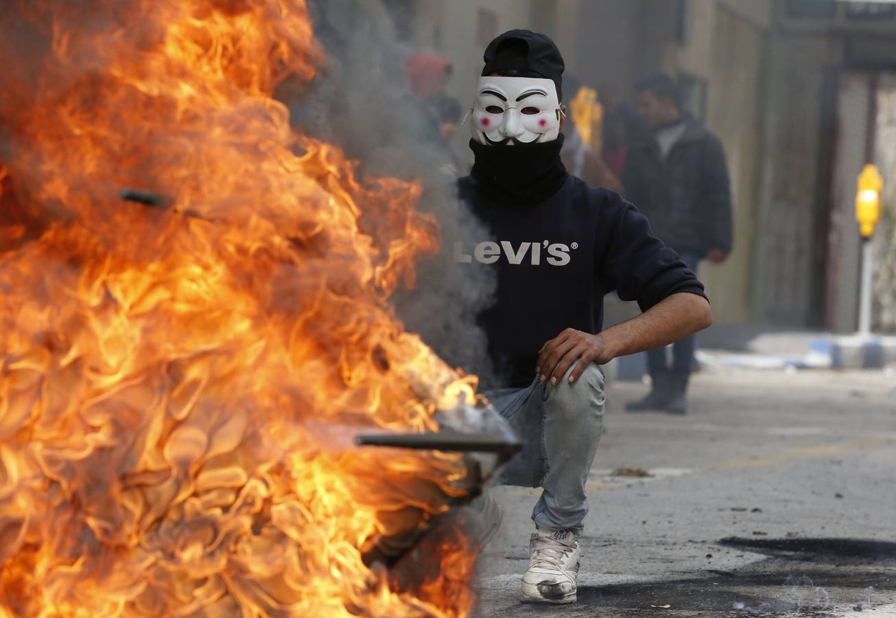 Un joven palestino con una máscara de Anonymous y una sudadera de una marca estadounidense, frente a una hoguera, durante un enfrentamiento contra tropas israelíes en Hebrón, tras el reconocimiento de Jerusalén como capital de Israel por parte de Donalg Trump.