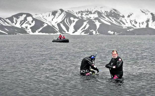 Dos investigadores se sumergen en el agua hasta la cintura protegidos por sus trajes de neopreno.