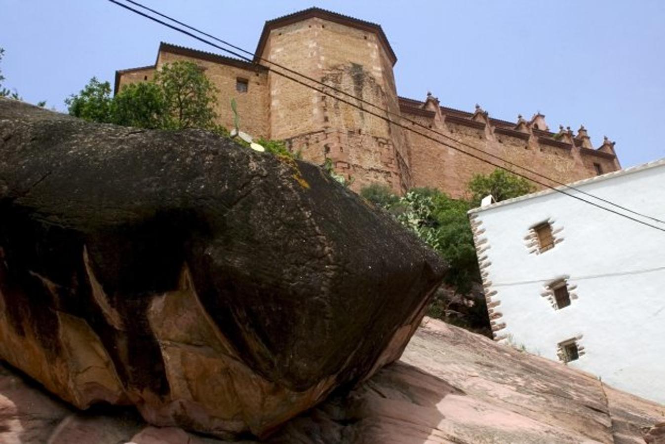 La Roca Grossa de Vilafamés. En mitad del pueblo, dando la bienvenida de camino al casco antiguo, está la Roca Grossa. Un particular Monumento de Interés Local de más de 2.000 toneladas que se ha convertido en un gran reclamo turístico. Muchas leyendas hablan sobre el procedimiento de esta mole con una inclinación de 34 grados sobre el estrato, pero una de las historias más curiosas es la que da nombre a los habitantes de Vilafamés. Cul Roig se les llama, ¿por qué? Cuentan que hace muchos años, los vecinos del pueblo decidieron trasladar los edificios, asentado sobre el monte, hasta un terreno más llano. El método empleado, atarlos con fuertes cuerdas y tirar de ellas. Pero, rozaron con la Roca Grossa que se encontraba a medio camino y resbalaron en el barro rojizo, con tan mala pata, que cayeron sentados sobre el fango y se ensuciaron las posaderas.