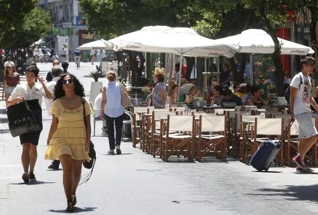 Varios ciudadanos caminan por la ciudad en un día soleado. 