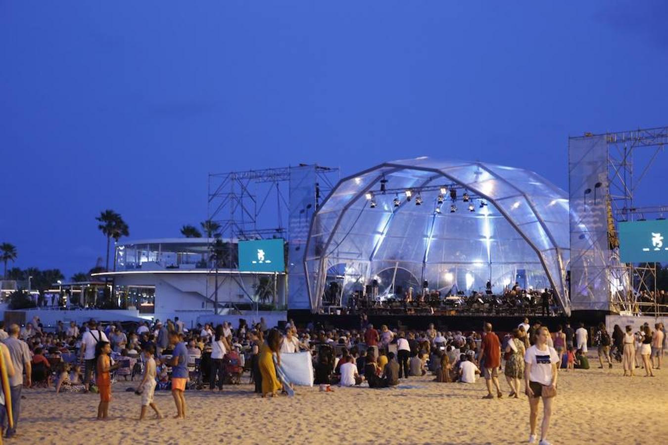 La Orquesta de Valencia hace historia junto al mar. Por primera vez, cierra la temporada en la playa de Las Arenas en un espectáculo para más de 1.000 personas. Un escenario de 300 metros y una cúpula transparente sirve de foco de atracción para el numeroso público congregado en la noche de este viernes en la playa. El concierto se ha bautizado con el nombre de 'Música i Aigua amb l'Orquesta de València'.