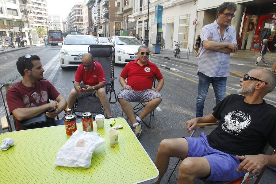 La huelga indefinida de taxistas en Valencia tiene como epicentro la calle Colón de Valencia. Allí, decenas de vehículo blancos están aparcados mientras los conductores tienen puesta toda la atención en la sede de Delegación del Gobierno. El único carril abierto es por el que circulan los autobuses de la EMT ante los taxistas que sentados en sillas plegables comentan, protestan y hace sonar el claxon. Unos conductores comparten café ante una mesa, mientras otros se muestran nerviosos con un cigarro en la mano. Ante la hora de comer, panes para los presenten y hasta se ha empezado un jamón entero. Las botellas de agua no han faltado ante las altas temperaturas que se registran en el centro de la ciudad.