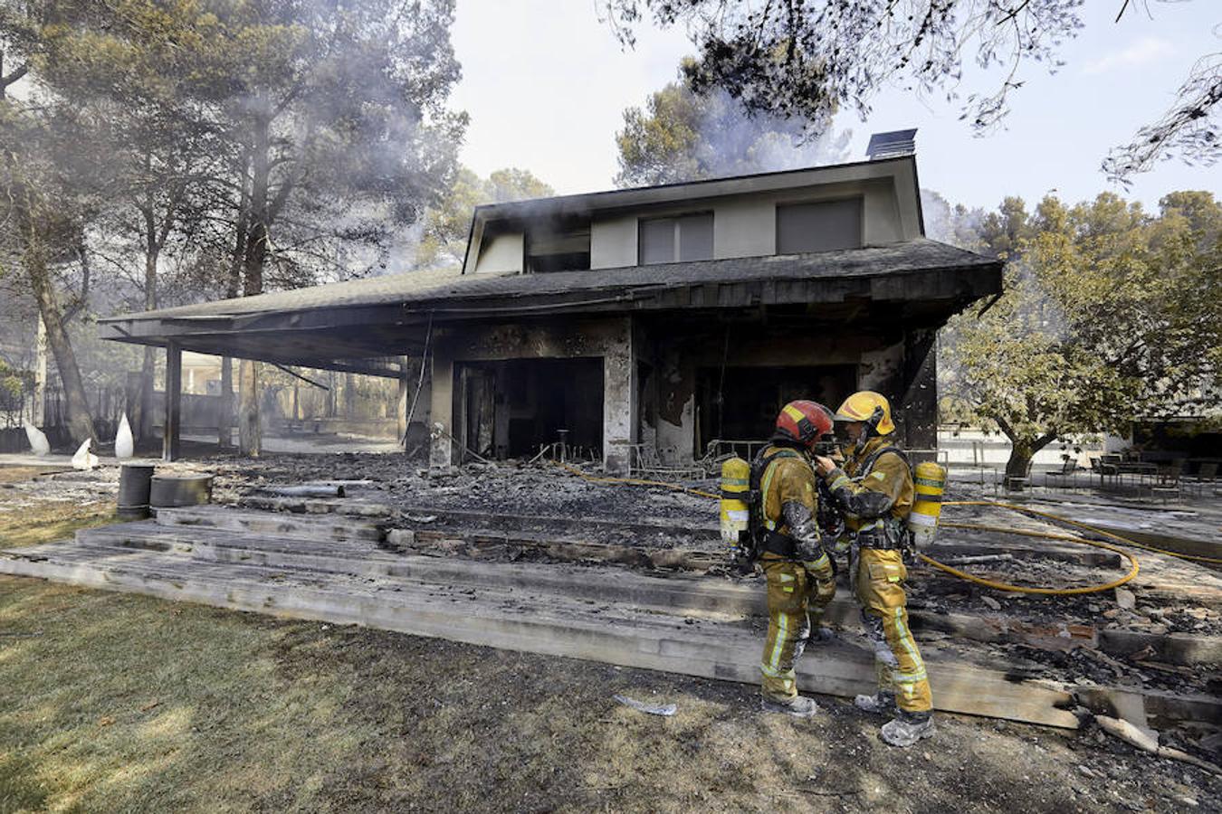 Dos bomberos conversan ante una de las viviendas afectadas por el incendio forestal de Llutxent en la zona de la Marxuqera (Gandía) 