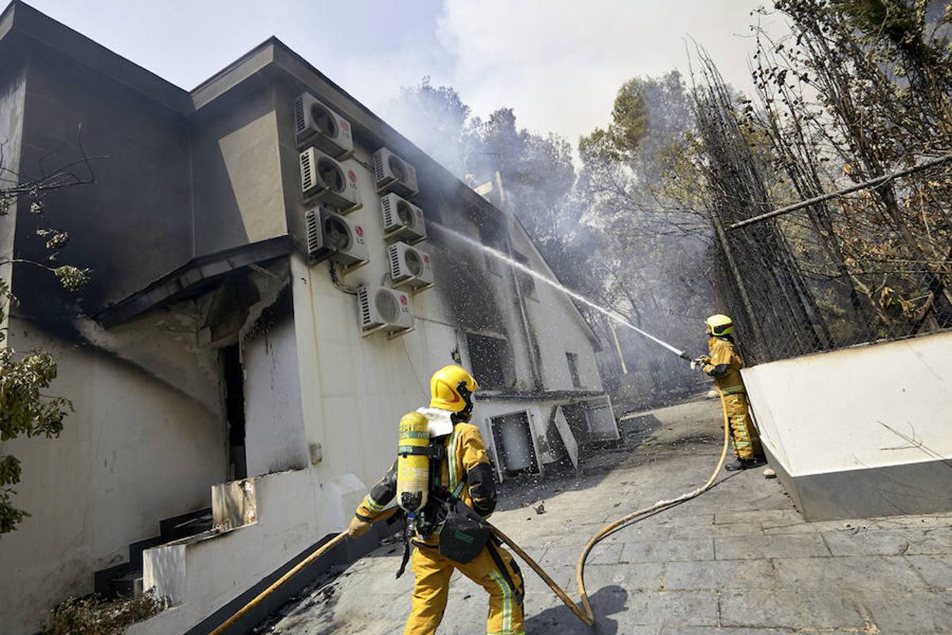 Dos bomberos refrescan el interior de una de las viviendas afectadas por el incendio forestal de Llutxent en la zona de la Marxuqera 