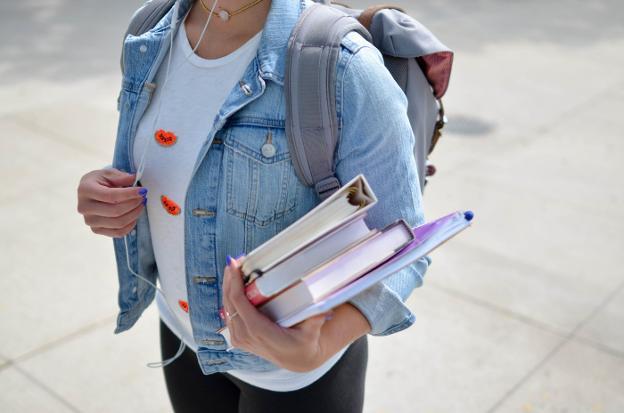 Una joven con varios libros y materiales antes de entrar en una clase. 