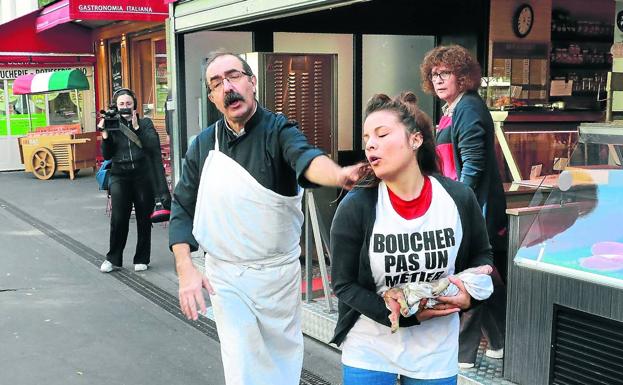 Un carnicero francés despacha de su negocio en París a una activista del grupo radical Abolición Contra la Carnicería que lleva en brazos un lechón muerto.