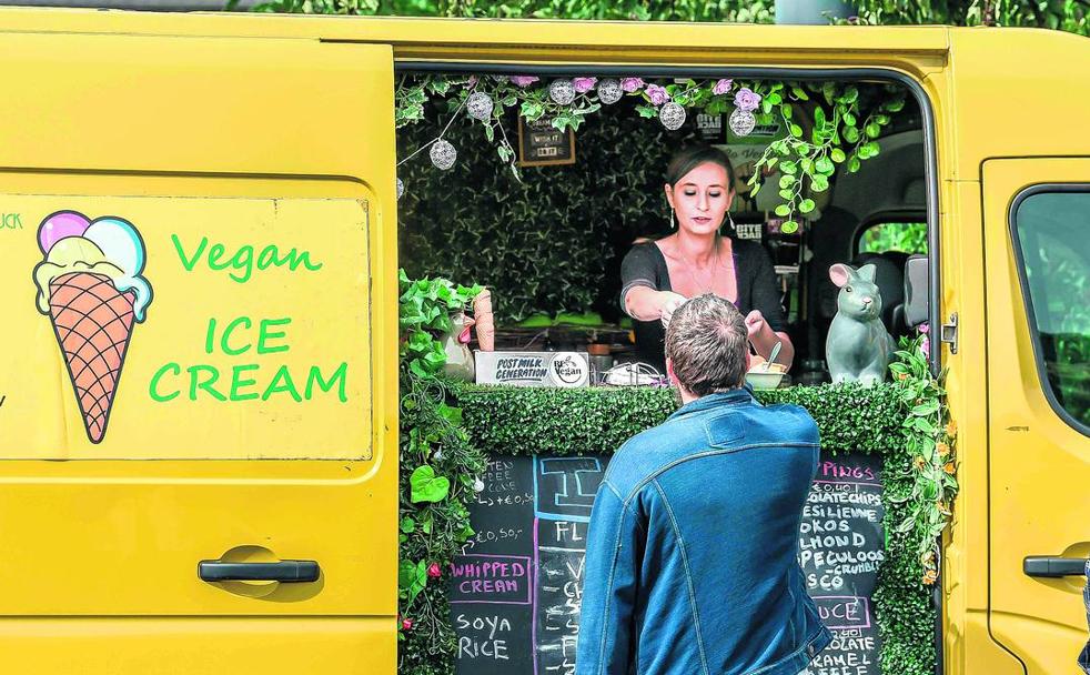 Una mujer sirve un helado elaborado con ingredientes vegetales a un cliente desde un puesto ambulante en un festival vegano en Francia.