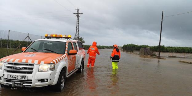 Dos miembros de Protección Civil avanzan con dificultad en una carretera inundada por las lluvias torrenciales caídas ayer sobre Tavernes de la Valldigna.