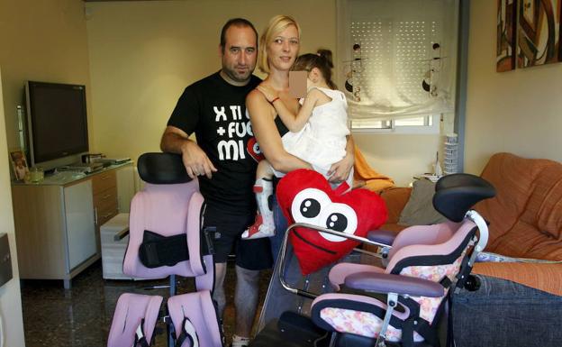 Los padres de Alba, con la pequeña, junto a dos sillas a medida que un equipo médico de Bélgica diseñó para ayudarla. 