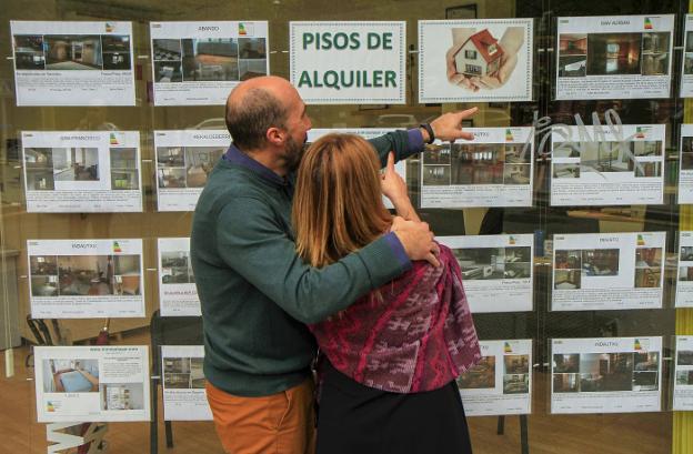 Una pareja observa las ofertas de casas en el escaparate de una inmobiliaria. 